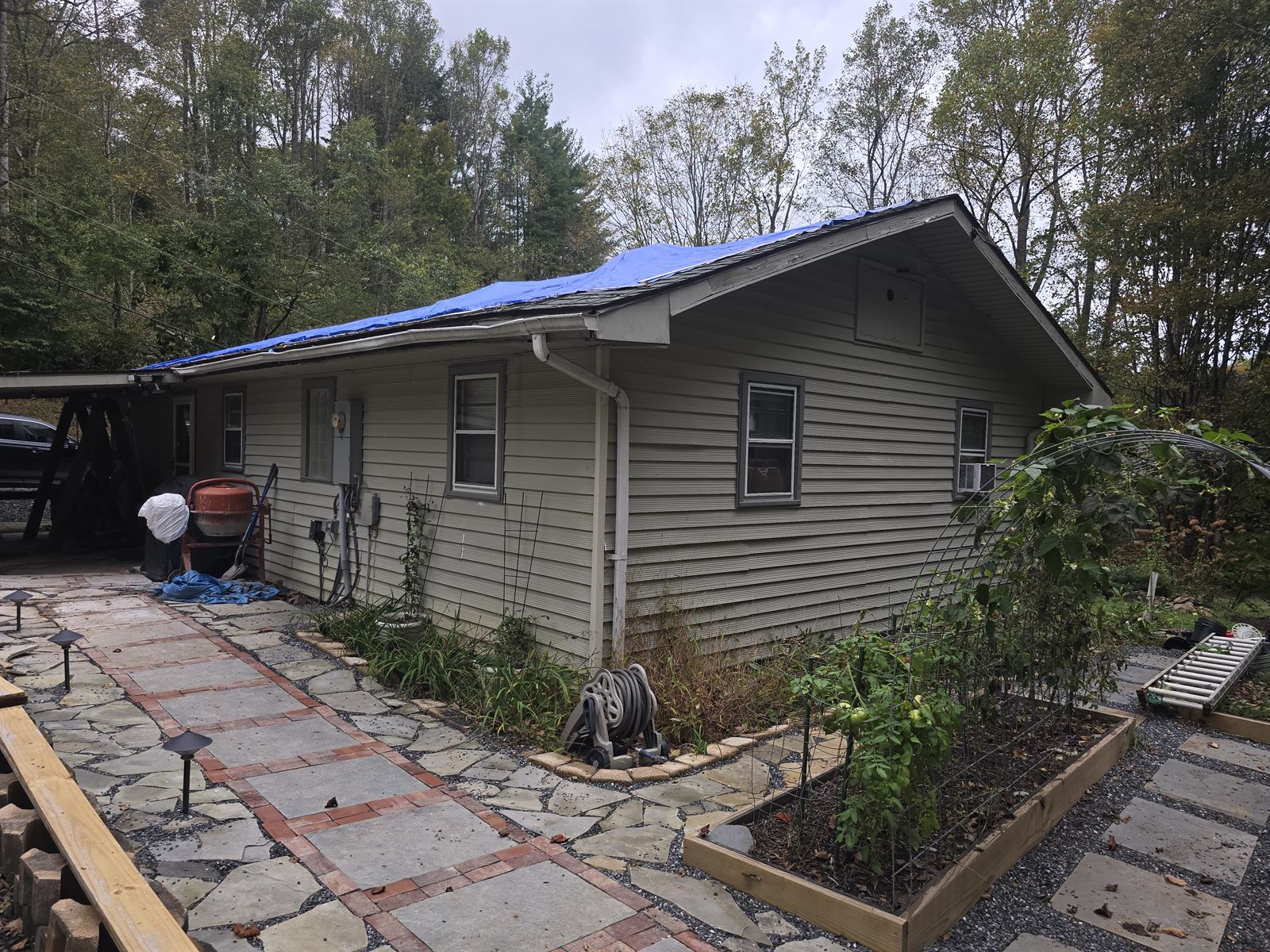 Home exterior before — storm-damaged, tarped roof and aging siding